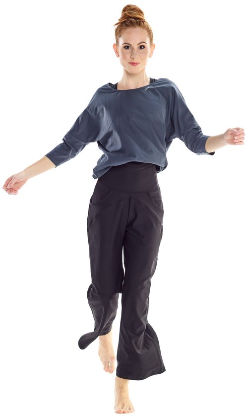 Vrouw in donkergrijze top en zwarte broek, springend, met blote voeten.