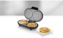 Open dubbele pancakemaker met 2 gebakken pancakes, naast een stapel pancakes op een wit bord.