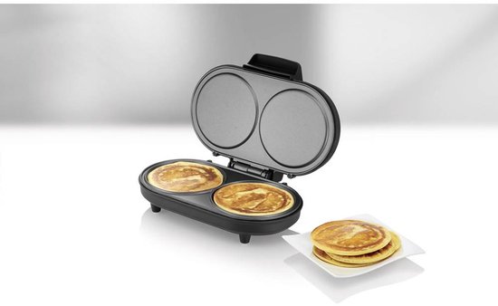 Open dubbele pancakemaker met 2 gebakken pancakes, naast een stapel pancakes op een wit bord.