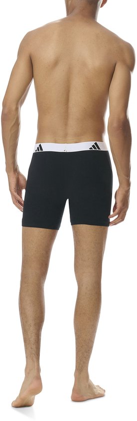 Model van achteren gezien in zwarte boxer briefs met witte tailleband en zwart Adidas-logo.