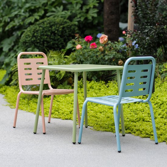 Een roze en een blauwe kinderstoel staan naast een groene kindertafel in een tuin.