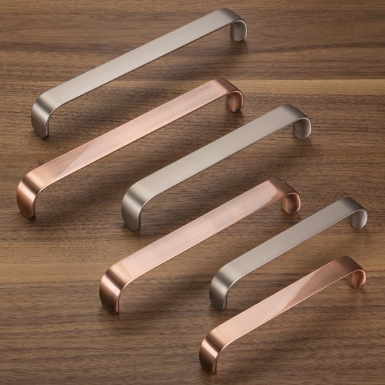 Vijf gebogen meubelgrepen, afwisselend zilverkleurig en koperlook, liggend op een houten ondergrond.