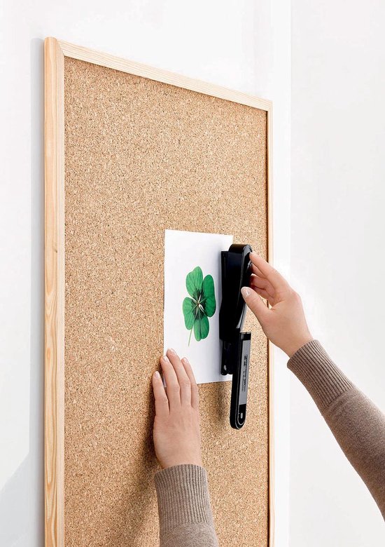 Handen gebruiken een zwarte nietmachine op een prikbord met klaverblad.