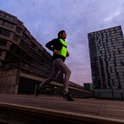 Man joggend in de stad met een fluoriserend geel reflectiehesje over een zwarte jas.
