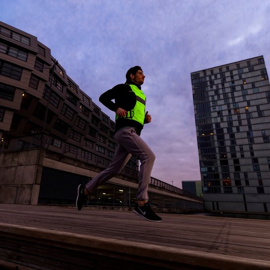 Man joggend in de stad met een fluoriserend geel reflectiehesje over een zwarte jas.
