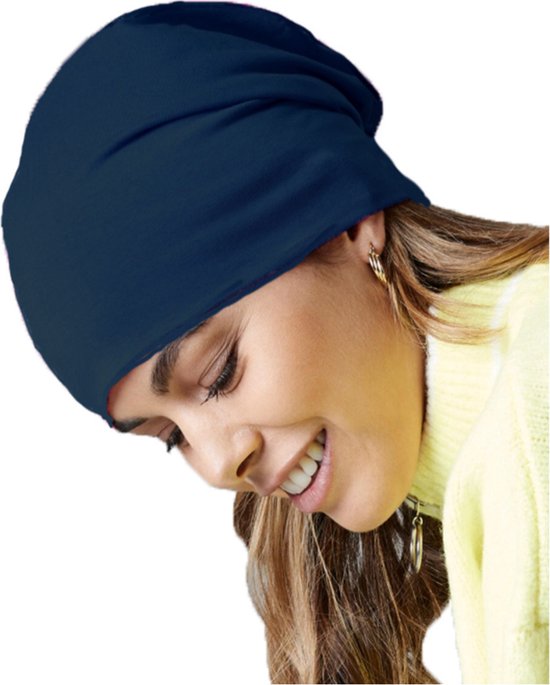 Een vrouw met lang blond haar draagt een donkerblauwe beanie en een gele coltrui. Ze draagt gouden oorbellen.