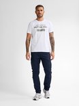 Man in volledig donkerblauwe cargobroek en witte t-shirt met tekst.