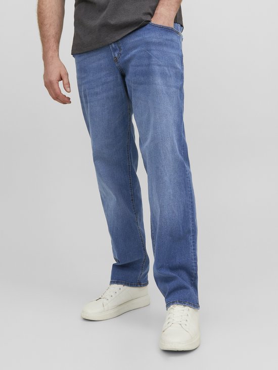 Close-up van de benen van een man die een blauwe jeans en witte sneakers draagt.