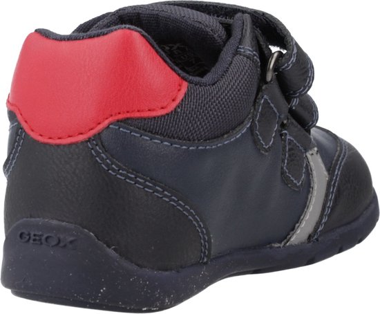 Donkerblauwe lage sneaker, achterkant met rode accenten, klittenbandsluiting en grijze details.