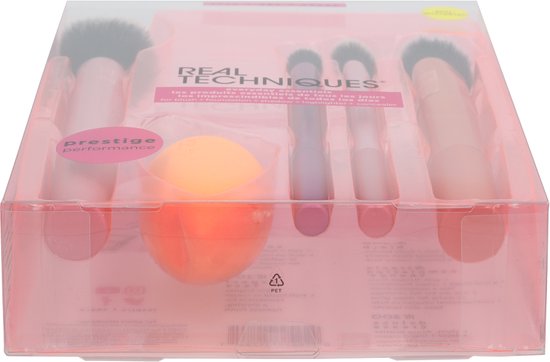 Een doorschijnende verpakking met een Real Techniques kwastenset, inclusief oranje spons en diverse roze, paarse en oranje kwasten.