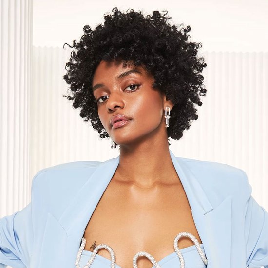 Model met natuurlijk krullend haar, draagt een lichtblauwe blazer en een top met parels.