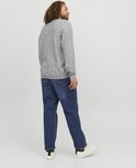 Man met krullend haar, van achteren gezien, draagt een lichtgrijs gemêleerde sweater en een spijkerbroek van blauw denim.