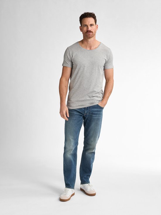 Man met grijze T-shirt met ronde hals en blauwe jeans, hand in de zak.