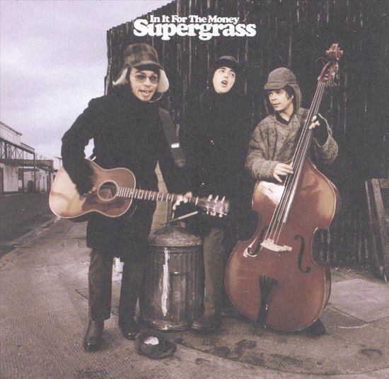 Drie mannen in winterkleding staan buiten met een akoestische gitaar, een basgitaar en een mandoline. Supergrass staat bovenaan.