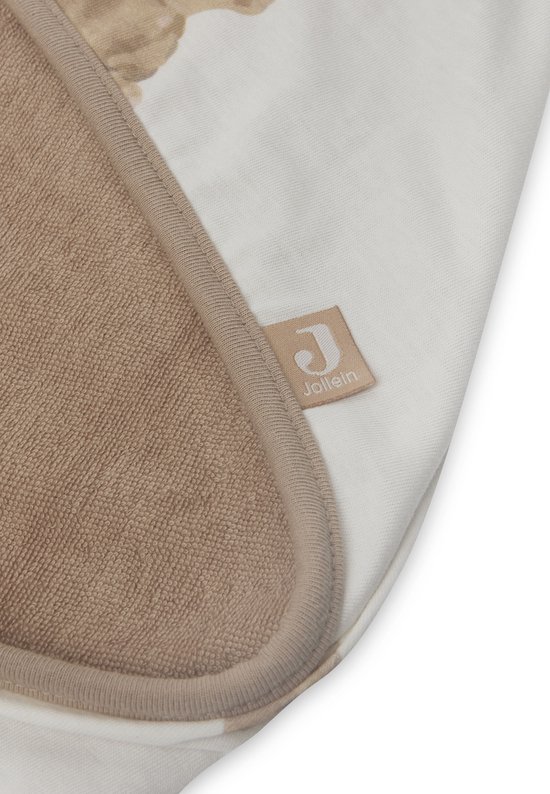 Détail d'une cape de bain blanc cassé avec intérieur marron en tissu éponge et bordure beige. Le logo Jollein est visible.