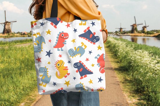Une femme porte un sac blanc à motif de dinosaures et d'étoiles rouges, bleus et jaunes, sur un chemin près de moulins à eau.