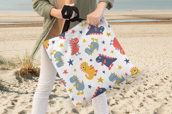 Une femme sur la plage porte un sac blanc à motif de dinosaures et d'étoiles rouges, bleus et jaunes.