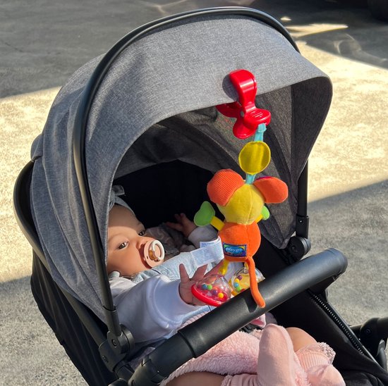 Een baby in een kinderwagen kijkt naar Mimsy de Muis, een gele knuffel met oranje lijf, groene armen en rode oren met stippen.