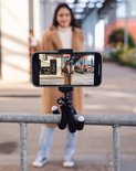 Een smartphone op een flexibel statief, waarop een vrouw met een bruine teddy jas te zien is.