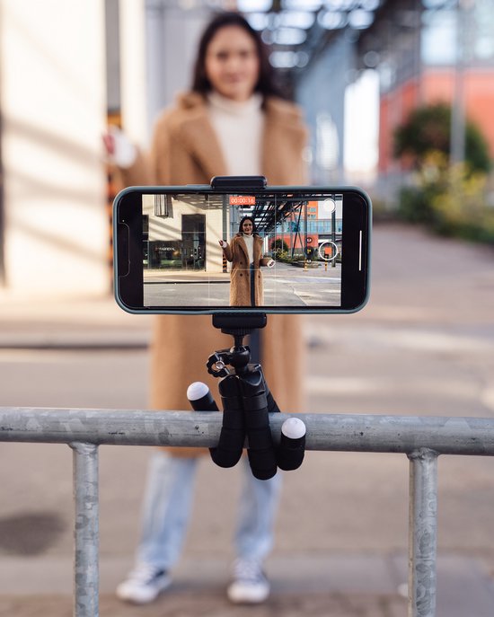Een smartphone op een flexibel statief, waarop een vrouw met een bruine teddy jas te zien is.