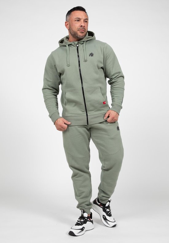 Man in een complete lichtgroene trainingsset van Gorilla Wear: hoodie met rits en joggingbroek. Hij draagt witte sneakers.