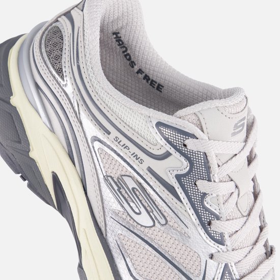 Detail van de zijkant van een zilverkleurige Skechers Slip-Ins sneaker met "Hands Free" op de binnenzool.