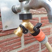 Messing kraanverdeler met zwarte hendels, aangesloten op een kraan en een rode tuinslangkoppeling, op een bakstenen muur.