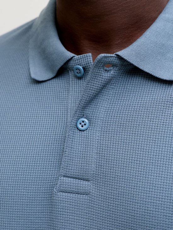 Detailopname van de kraag en knopen van een blauw poloshirt met wafeltextuur.