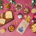 Borrelplank met kaas, chips, noten, koekjes, drinken en worst op een roze achtergrond met kerstdecoratie.