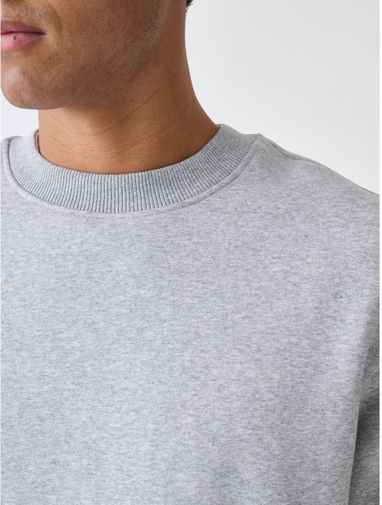 Close-up van een grijze sweater met ronde hals in ribbelstructuur, gedragen door een man.