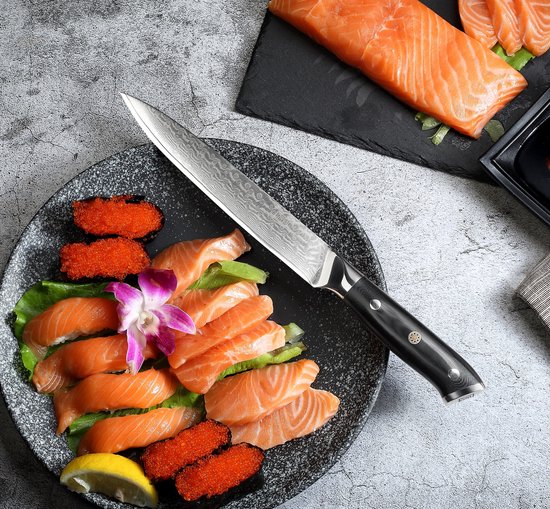 Een Paudin mes met damaststalen lemmet ligt op een bord met zalmsashimi en viseieren. Gekookte zalmfilet ligt ernaast.