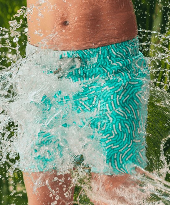 Close-up van turquoise zwembroek met wit patroon, gespetterd met water.