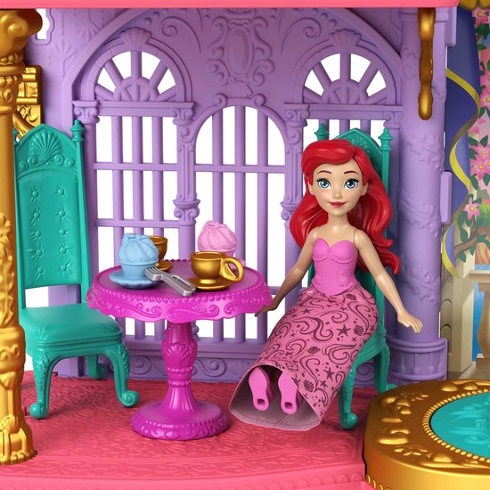 Ariel de zeemeermin in een roze jurk met gouden details, zittend aan een tafel in een kasteel
