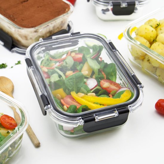 Glazen vershouddoos met salade, omringd door andere bakjes met eten.