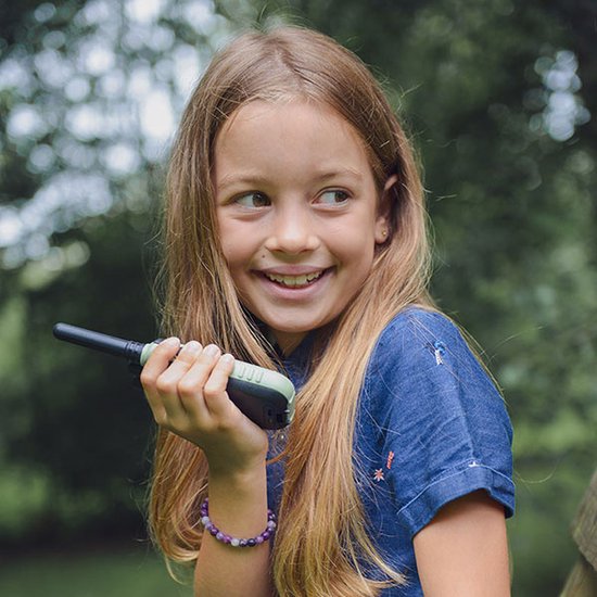 Meisje met lang blond haar, die een groene Kidywolf KIDYTALK walkietalkie vasthoudt.