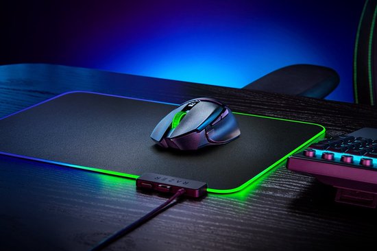 Zwarte Razer Basilisk V3 X Hyperspeed muis met groene scrollwheel op zwarte muismat met gloeiende groene rand.