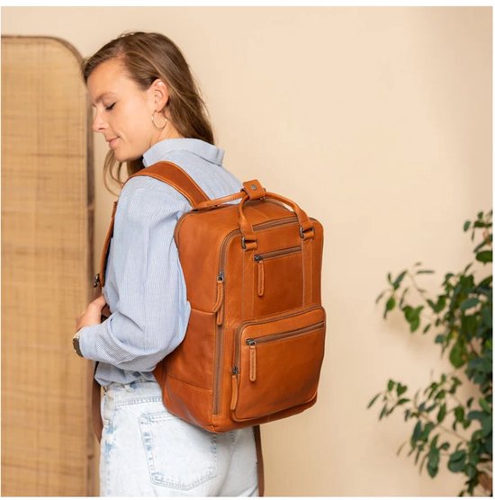 Een vrouw draagt een cognac kleurige leren rugzak. De rugzak heeft meerdere ritsvakken.
