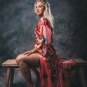 Model zittend op houten bankje in lange koraalrode satijnen kimono met bloemenprint.