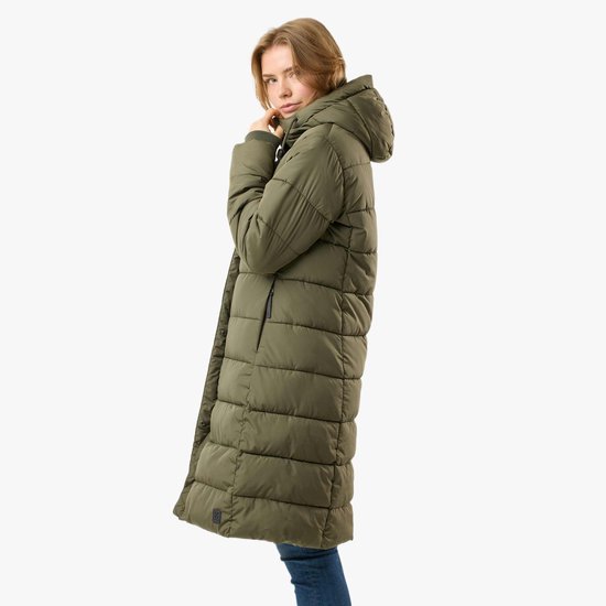 Zijaanzicht van een lange groene gewatteerde jas met capuchon, gedragen door een model met spijkerbroek. Ze trekt aan de capuchon.