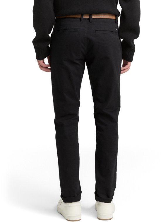 Man van achteren gezien, draagt een zwarte chino met bruine riem, trui en witte sneakers.