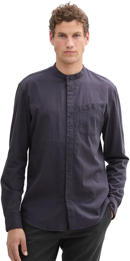 Man met donkerblauw overhemd met opstaande kraag en donkere broek.