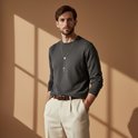 Man met donkergrijs trui en lichtbeige broek, staat met handen in zakken, draagt rozenkrans.