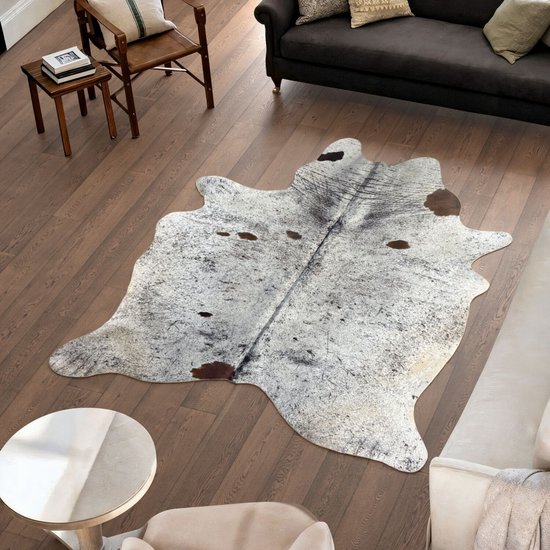 Koeienhuid vloerkleed op een houten vloer in een woonkamer, met bruine en witte vlekken.