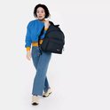 Vrouw met krullend haar in een blauwe trui en jeans draagt een donkerblauwe Eastpak rugzak.