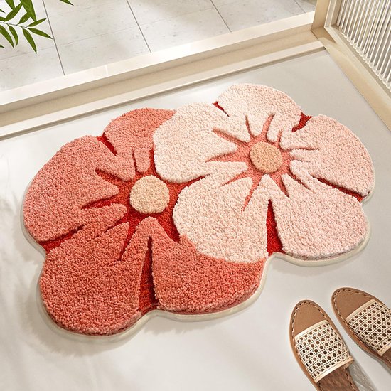 Un tapis de bain rose et rouge en forme de fleur, composé de deux parties florales avec une fleur plus grande et une plus petite au centre. L'arrière-plan est gris clair.