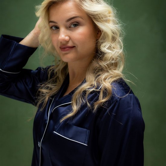 Close-up van model met blond haar, draagt een donkerblauwe satijnen pyjamajas met witte biesjes en knoopsluiting.