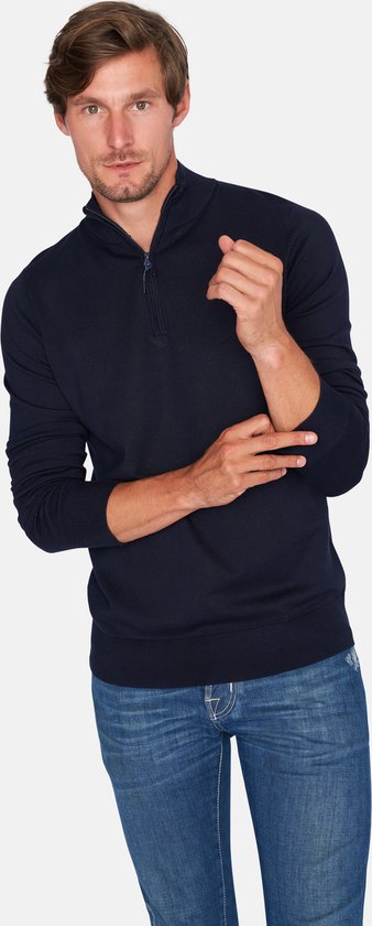 Man met donkerblauwe trui met rits tot de borst en jeans.