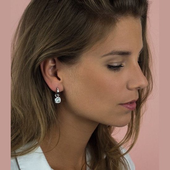 Model draagt een zilveren oorbel met een vierkante, witte hanger.