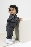 Baby in donkergrijs joggingpak met ronde hals, leunend tegen een witte kubus.
