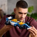Een man houdt een Lego Williams Formule 1 auto, met gele en blauwe kleuren.